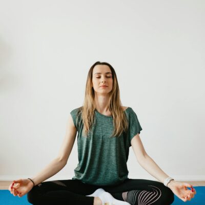 Calm slim female in sports clothes sitting with crossed legs in Padmasana pose on yoga mat while meditating with closed eyes in flat