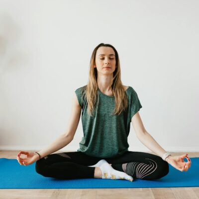 Serene blond lady in sportswear sitting with crossed legs and closed eyes while practicing yoga at home near potted plants